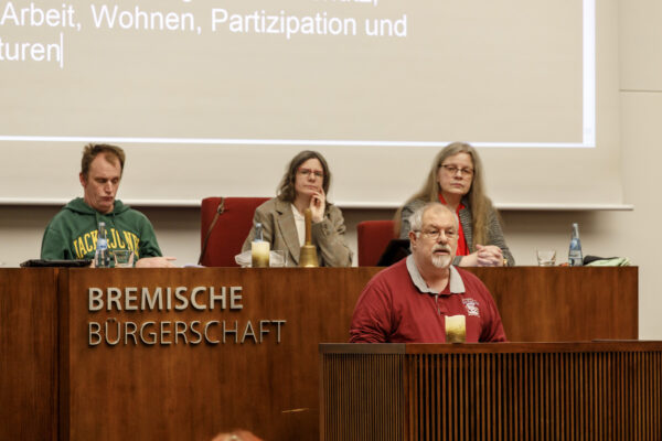 Udo Schmidt trägt seinen Leitantrag im Parlament vor. Hinter ihm das Präsidium mit Heiko Blohm, Victoria Ruppnow, Rosemarie Kovac